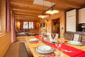 A wooden interior with a dining table set for four, a sofa, and a kitchen area.