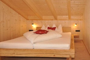 A wooden cabin room with a bed, two wall-mounted lights, and a wooden ceiling.