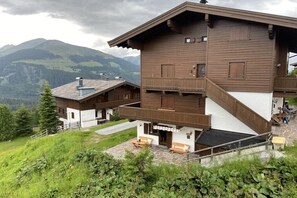 Un chalet à deux étages doté d’un balcon, d’une terrasse en pierre et surplombant un paysage montagneux.
