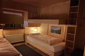 A wooden cabin room with bunk beds, a nightstand, a lamp, and a window with a view. - Alpine Bliss-Hochkrimml (Krimml)