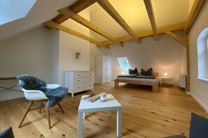 A loft bedroom with a sloped ceiling, wooden beams, a bed with pillows, a chair, a small table, and a window. - Zartwitzer Hütte Forest Lodge (Rechnlin)