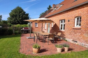 Une terrasse avec une table et des chaises, un barbecue et des plantes en pot.