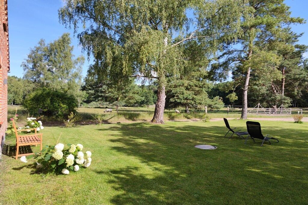 A grassy backyard with a large tree, a brick wall, and outdoor seating.