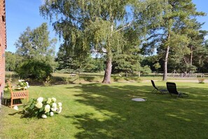 A grassy backyard with a large tree, a brick wall, and outdoor seating. - Zartwitzer Hütte Forest Lodge (Rechnlin)
