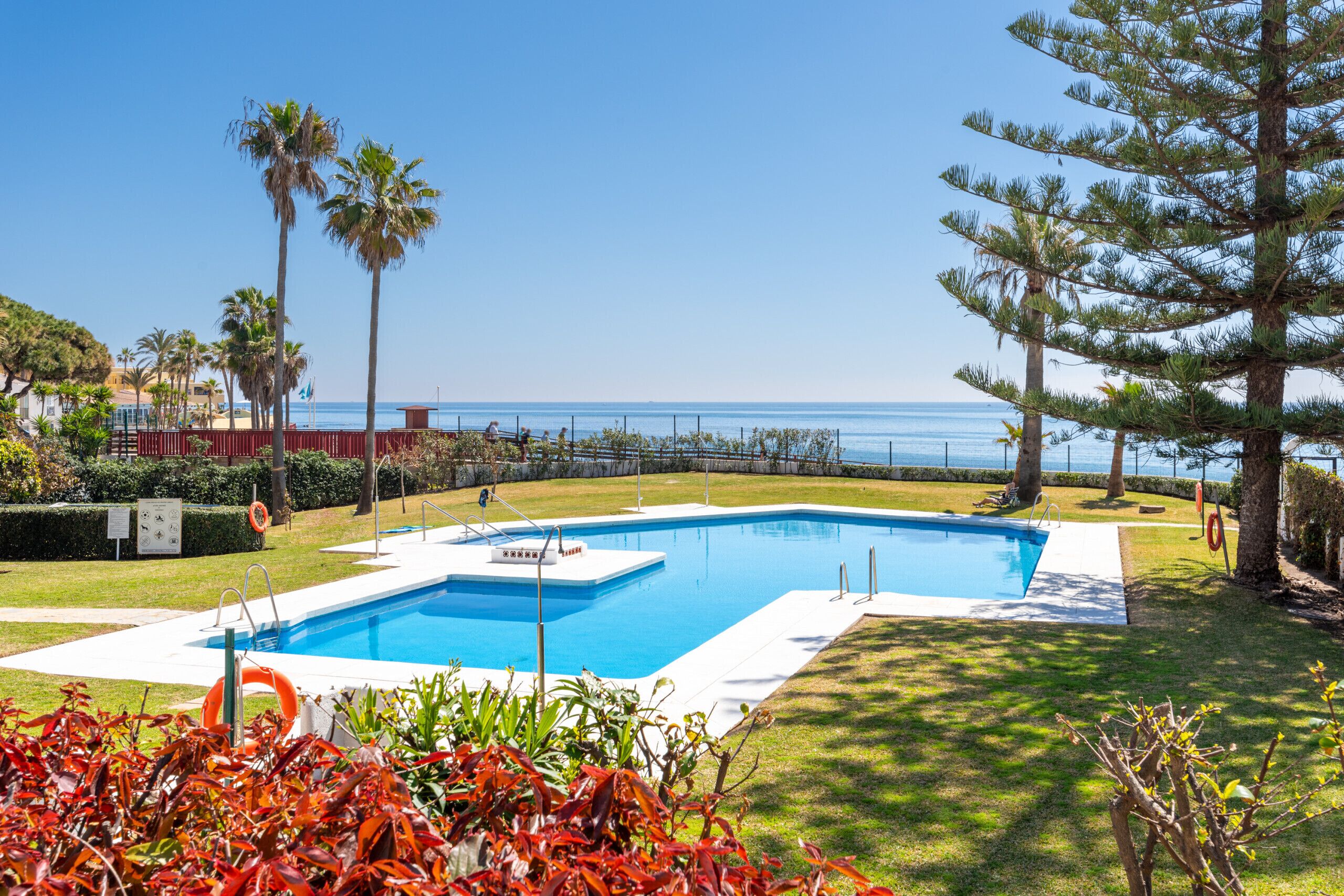 A rectangular swimming pool with a clear view of the sea in the background.