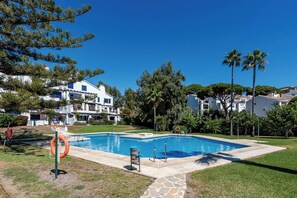 A swimming pool with a lifebuoy, surrounded by grass and trees, with buildings in the background. - Calahonda Beach III – Beachfront Apartment with Sea Views in Mijas Costa (Mijas Costa)