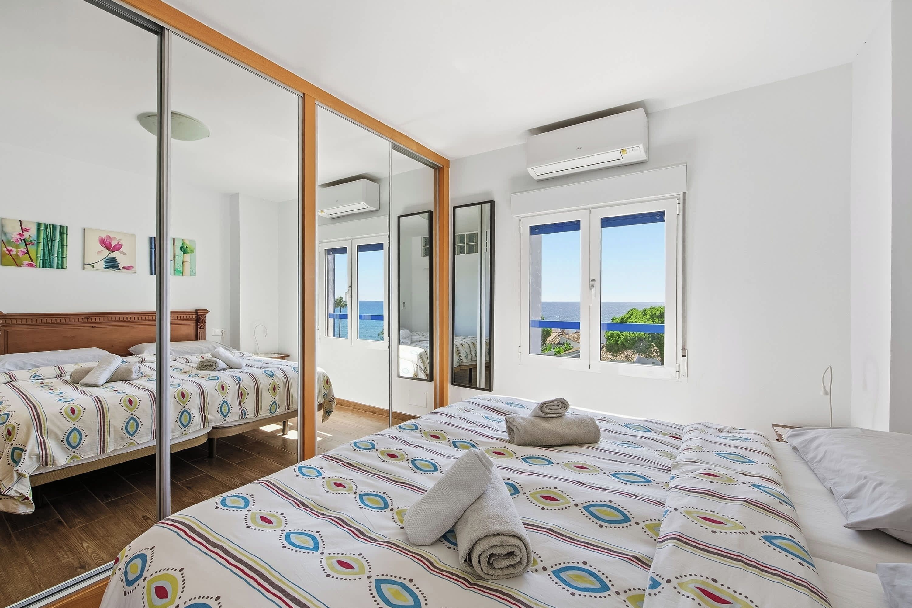 A hotel room with two beds, a large mirror, and a view of the sea.