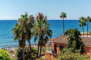 A coastal property with a view of the sea, palm trees, and a building with a tiled roof. - Calahonda Beach III – Beachfront Apartment with Sea Views in Mijas Costa (Mijas Costa)