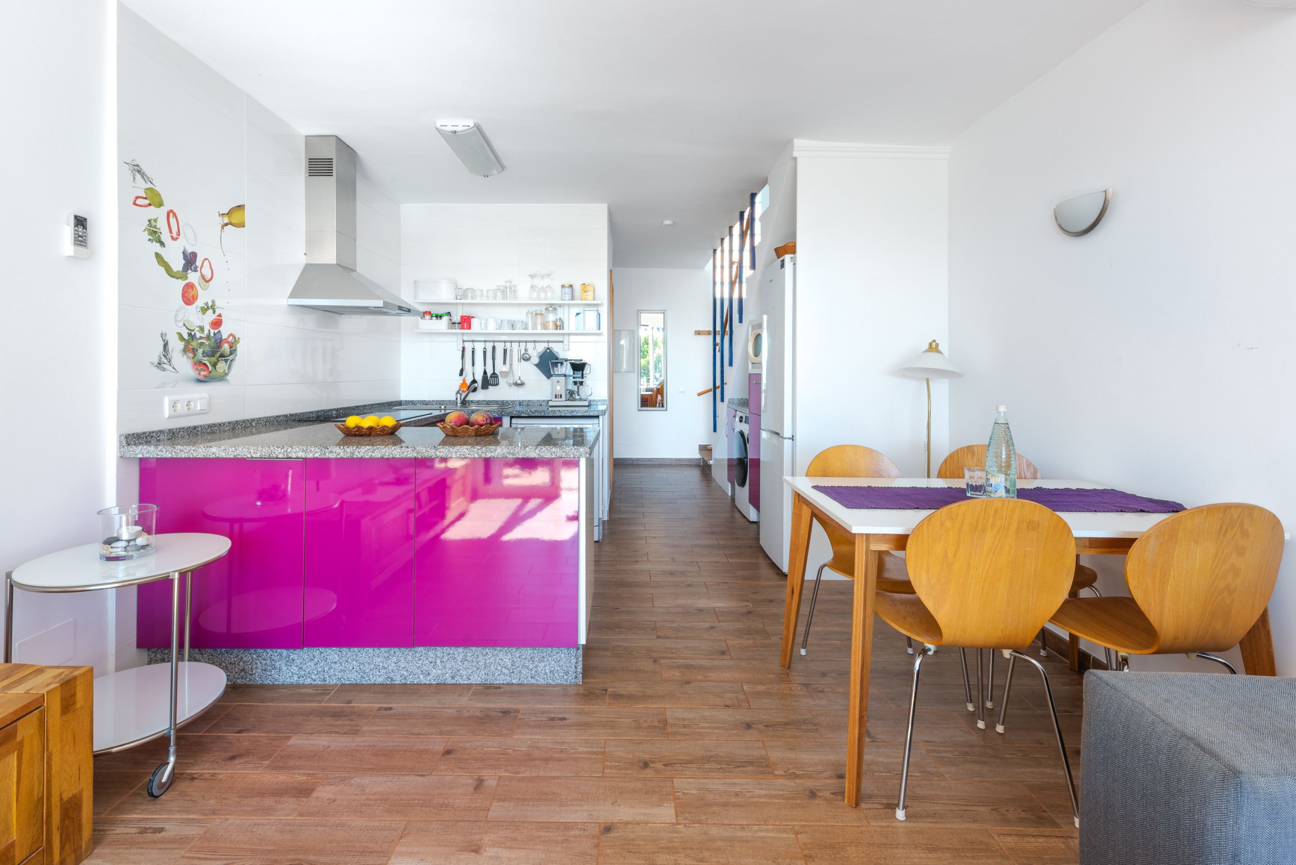 A modern kitchen with a central island, a dining area with wooden chairs, and a visible laundry area.