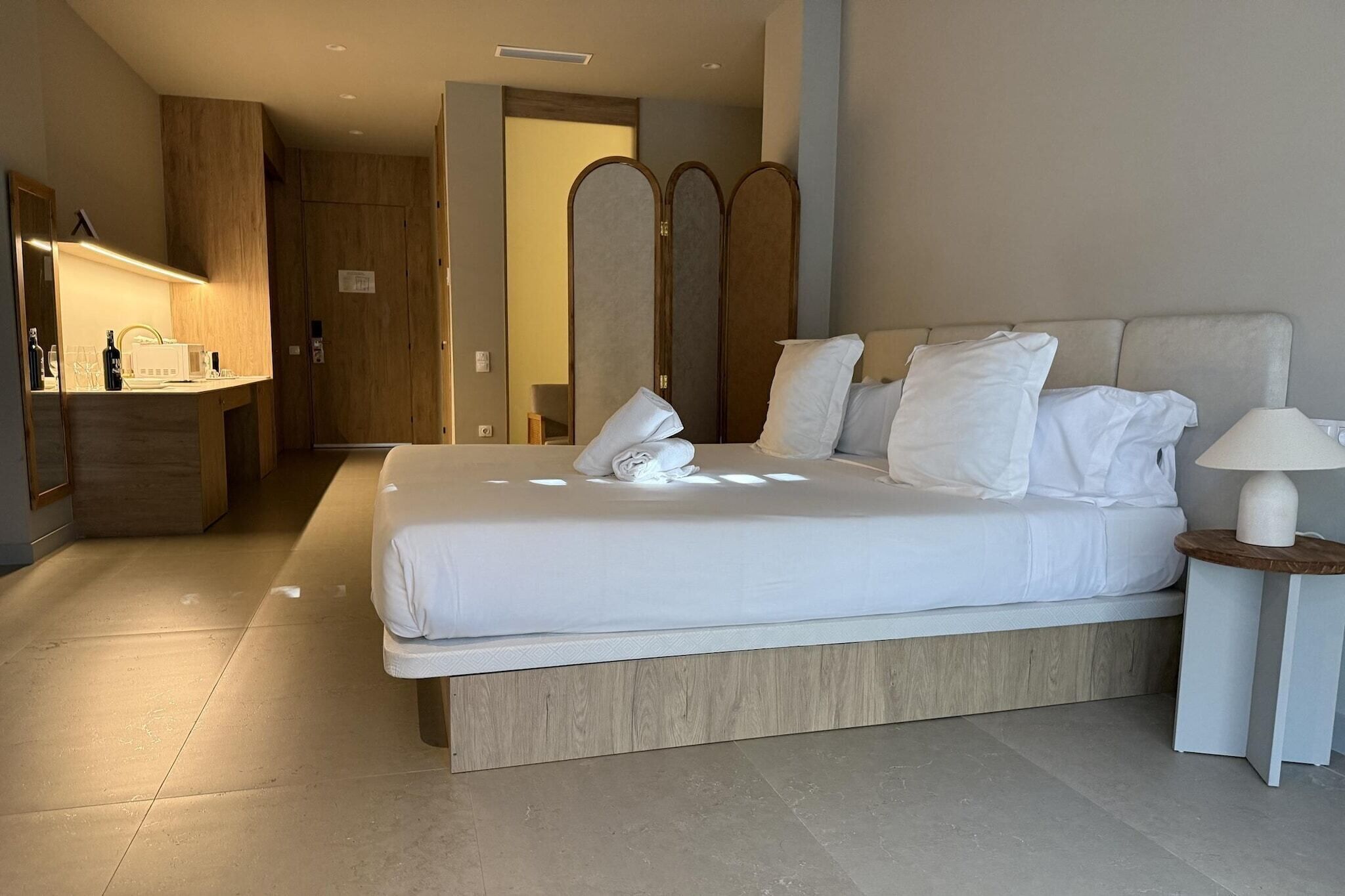Una habitación de hotel con una cama, una mesita de noche con lámpara, un espejo y un armario de madera.