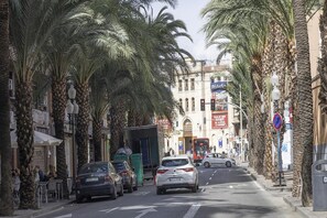 A street lined with palm trees and buildings, cars parked along the side, and a bus in the distance. - Apartment La Plaza 2 double standard (Alicante)