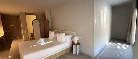 A hotel room with a large bed, a bedside table with a lamp, a mirror, and a view of a corridor.