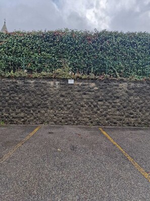 Un espace de stationnement bordé d’un mur en briques et d’une haie.