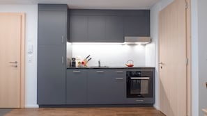 A compact kitchen with grey cabinets, a built-in oven, and a kettle on the countertop. - Brilliant apartment in Saxon for your getaway (Saxon)
