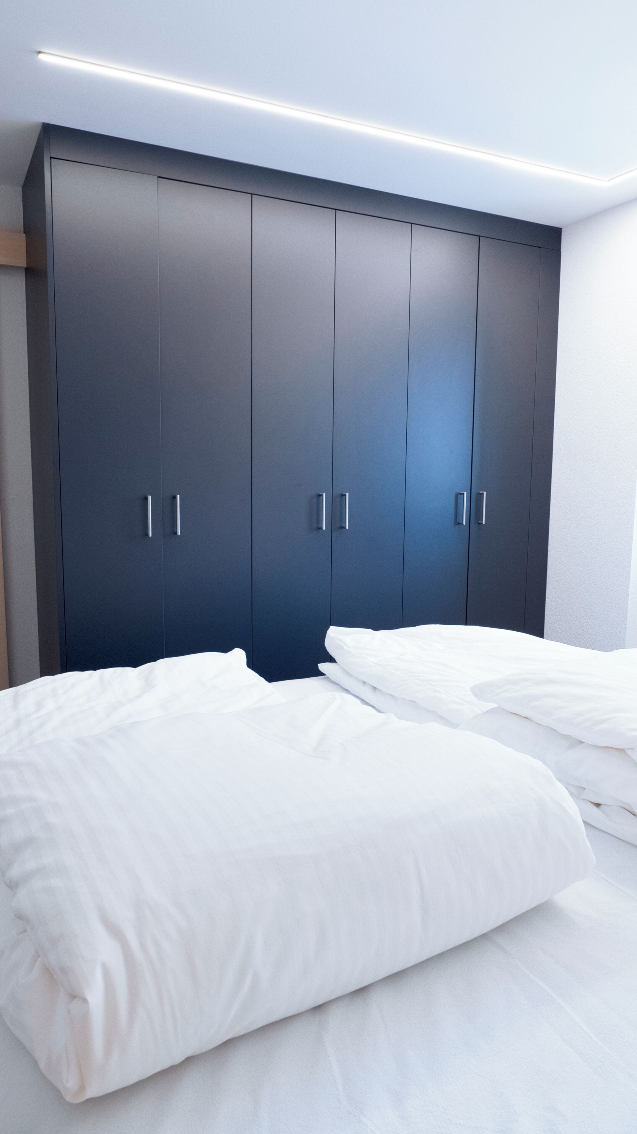 Une chambre avec une grande armoire sombre, deux lits avec du linge de lit blanc et un luminaire fixé au plafond.