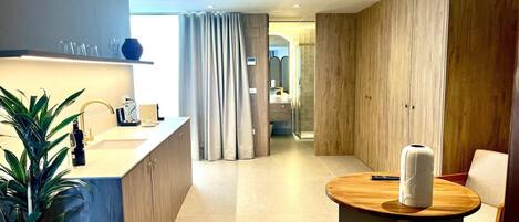 A modern hotel room with a wooden cabinet, a round wooden table, a potted plant, and a shower area.