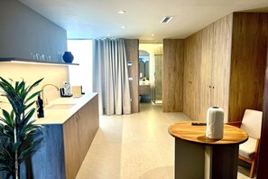 A modern hotel room with a wooden cabinet, a round wooden table, a potted plant, and a shower area. - Apartment La Plaza 2 Deluxe with Jacuzzi (Alicante)