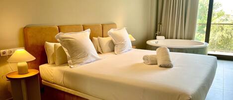 A hotel room with a bed, a nightstand with a lamp, a bathroom with a bathtub, and a window with curtains.