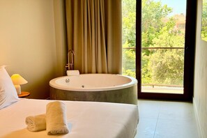 A hotel room with a large bathtub, a bed, a nightstand with a lamp, and a view of greenery outside. - Apartment La plaza 2 deluxe with balcony (Alicante)
