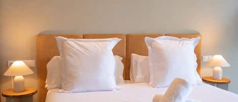 A neatly made bed with white linens and pillows, two bedside lamps, and a wooden headboard.