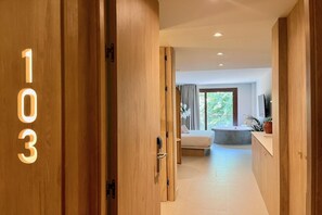 Ein Hotelzimmer mit großem Fenster, einem Bett, einem Badezimmer mit Badewanne und einer Holztür mit der Nummer 103.