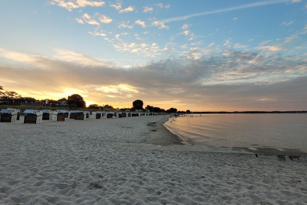 A beach with a row of beach huts and a calm sea under a partly cloudy sky.