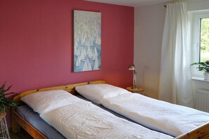 Een kamer met twee eenpersoonsbedden, een schilderij aan de muur, een bedlampje en een raam met gordijnen.