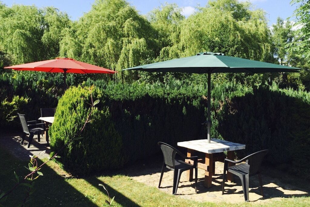 An outdoor patio with a table and chairs, two umbrellas, and dense foliage in the background.