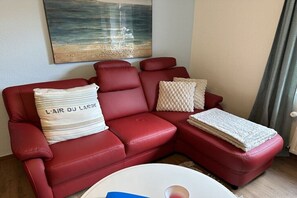 Ein rotes Ledersofa mit einem Kissen mit dem Aufdruck 'L'Air du Large' und einer gewebten Decke.