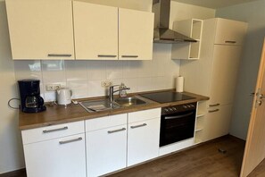 Een keuken met witte kastjes, een spoelbak, een fornuis en een koffiezetapparaat.