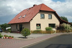 Ein zweistöckiges Haus mit rotem Ziegeldach, einer Ziegelaußenwand und einem kleinen Vorgarten mit Topfpflanzen.