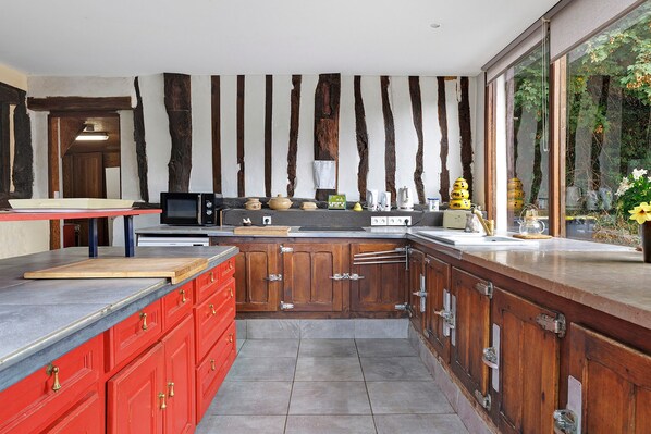 A kitchen with a modern design, featuring a large island, wooden cabinets, and a view of greenery outside.