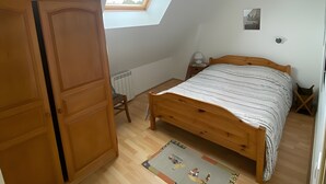 Ein Schlafzimmer mit schrägen Wänden, einem Oberlicht, einem hölzernen Bett, einem Nachttisch, einer Heizung und einer Tür.