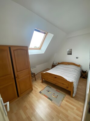 Een slaapkamer met een schuine kap, dakraam, houten bed, nachtkastje, radiator en een deur.