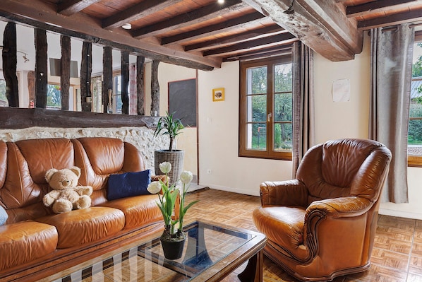 A room with a brown leather sofa, a brown leather armchair, a glass coffee table, and a potted plant.