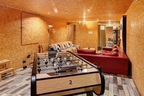 A room with a foosball table, a red sofa, and a wooden floor.