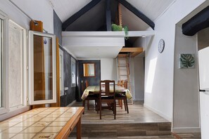 A dining area with a wooden table and chairs, a window with curtains, and a clock on the wall.