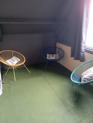 Een kamer met drie stoelen, waarvan er een een vogelmotief kussen heeft, een andere ook een vogelmotief kussen, en de derde een gestreept kussen.