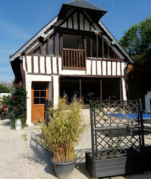 A two-story house with a balcony, a wooden door, and a large potted plant in the foreground.
