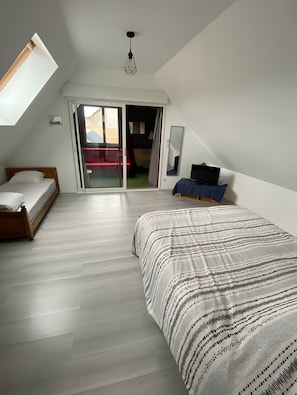 A bedroom with a bed, a desk, a chair, a wardrobe, a mirror, and a sliding glass door leading to an outdoor area.