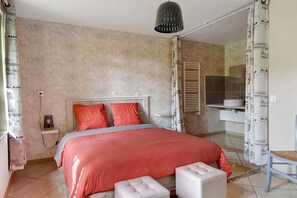 A bedroom with a bed, a bedside table, a lamp, a chair, and a bathroom visible through an open door.