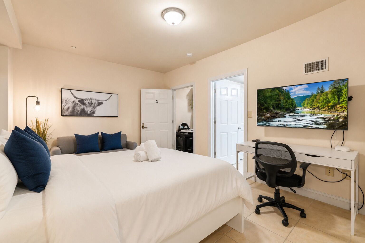 A hotel room with a bed, a desk, a chair, a TV, and a door.