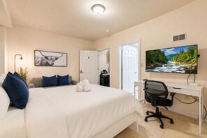 A hotel room with a bed, a desk, a chair, a TV, and a door.