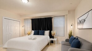 Quarto de hotel com uma cama grande, um sofá cinzento, uma mesinha e uma obra de arte na parede.