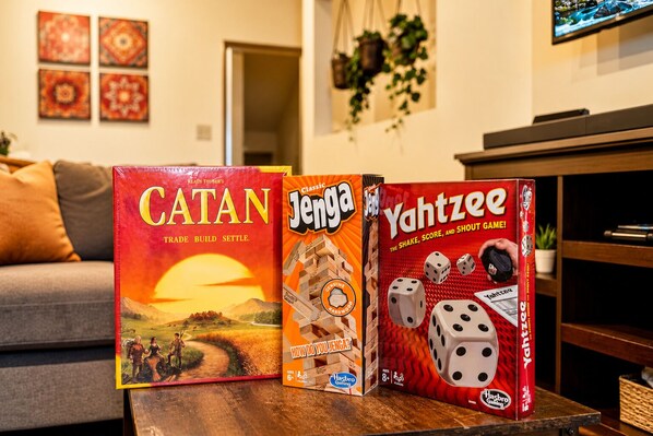 Three board games: Catan, Jenga, and Yahtzee, on a wooden table in a living room.
