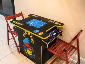 A gaming arcade table with a digital screen, joystick, and buttons, surrounded by red chairs.