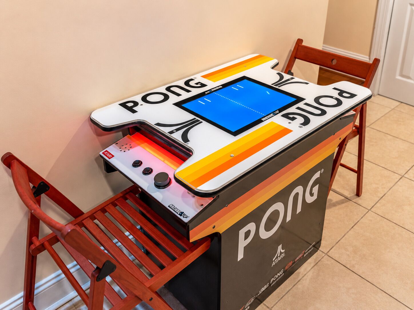 A Pong arcade game machine with a screen and control buttons, placed on a table with a chair beside it.