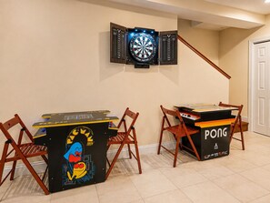 A room with a dartboard mounted on the wall, a ping pong table, and two wooden chairs.