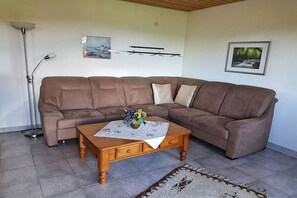 A living room with a brown sectional sofa, a wooden coffee table with a vase of flowers, and a floor lamp. - Holiday apartment with 1 bedroom (Missen-Wilhams)