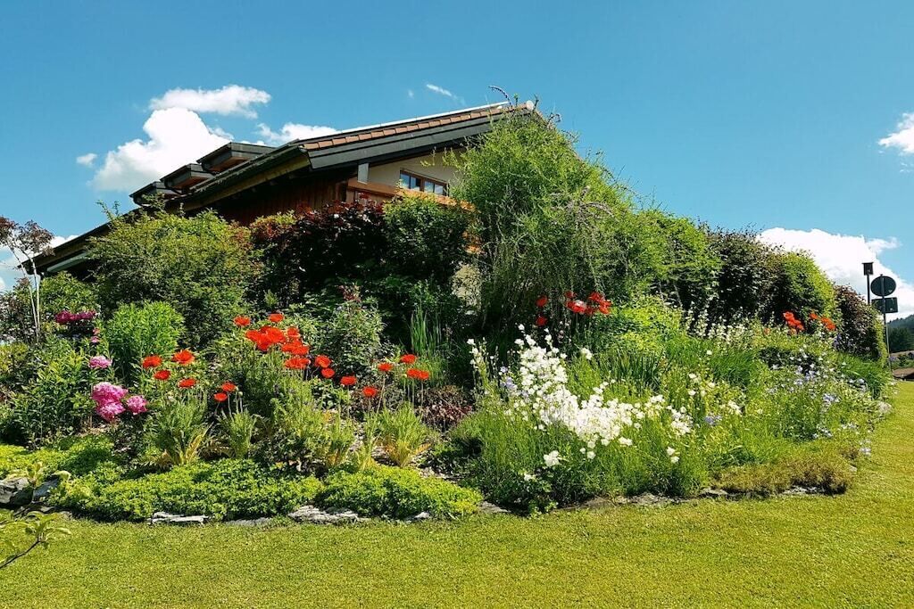 A house with a sloped roof, surrounded by a garden with various plants and flowers.